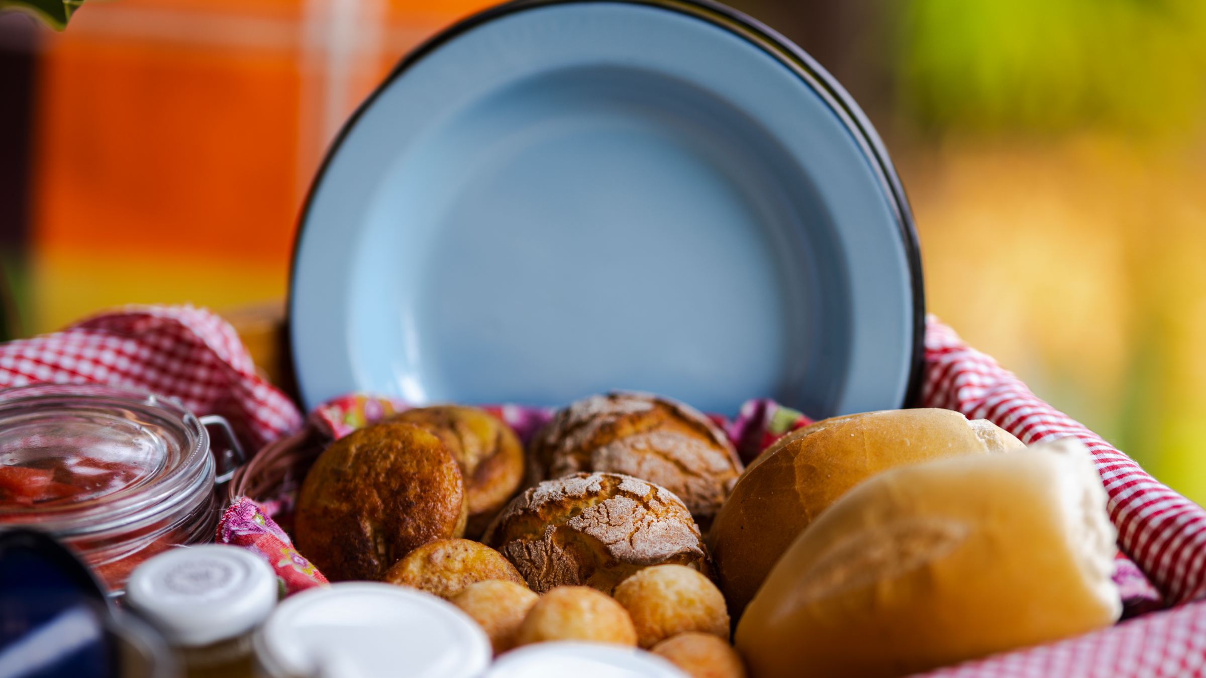 Cesto de pães e broinhas ao lado do prato azul, na bandeja do café