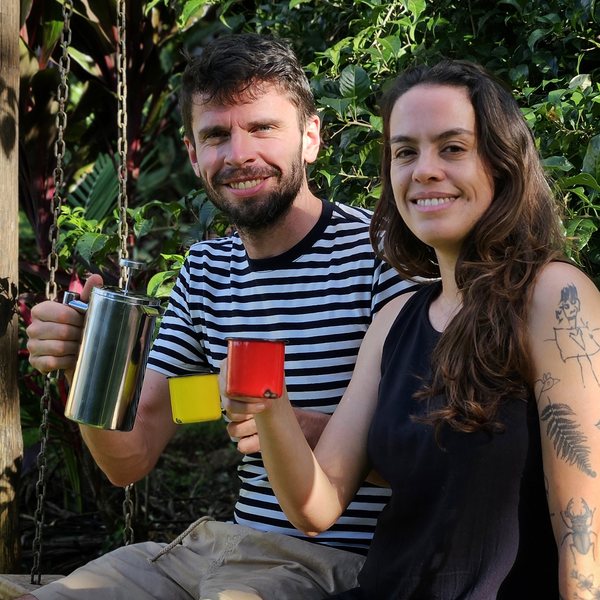 Os dois anfitriões sentados no balanço, com a cafeteira e as canecas na mão