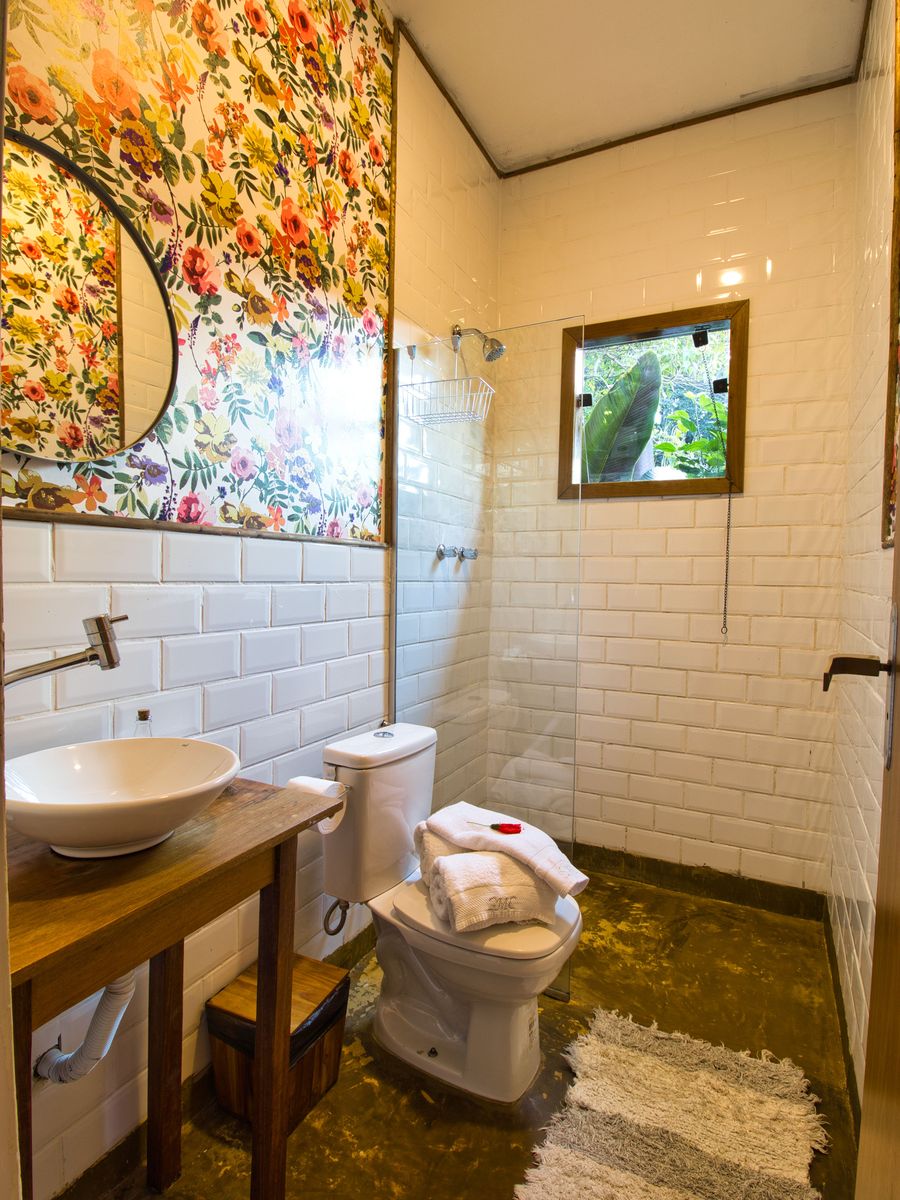 O banheiro da Casinha do Solar, de azulejo branco, com a cuba na bancada de madeira e a janelinha para o verde
