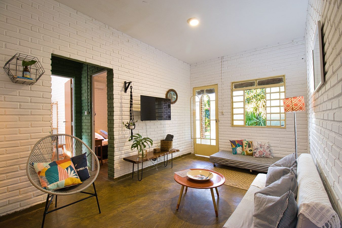 A outra ponta da sala da Casinha, com o futon, a porta amarela e a janela para o jardim