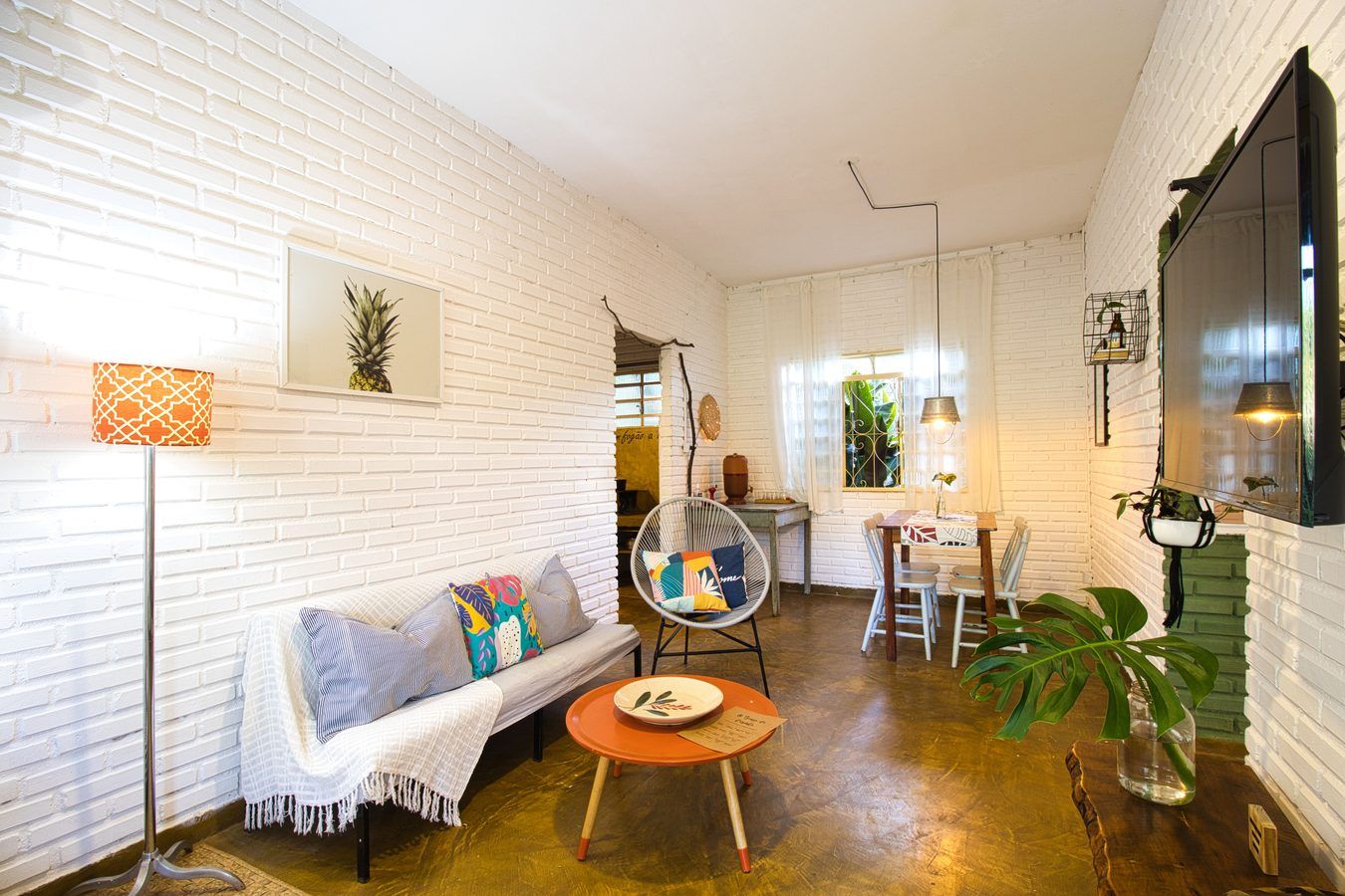 A sala da Casinha do Solar aberta: o sofá com almofadas, a poltrona de fio, a mesinha redonda e, ao fundo, a mesa de jantar com as cadeiras