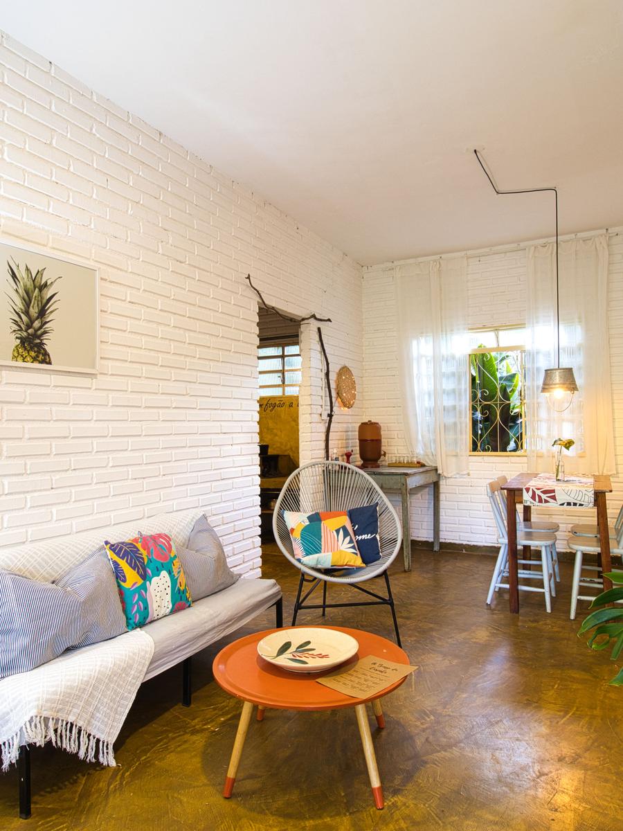 Sala da Casinha do Solar: parede de tijolo branco, sofá, poltrona suspensa e mesa de centro redonda