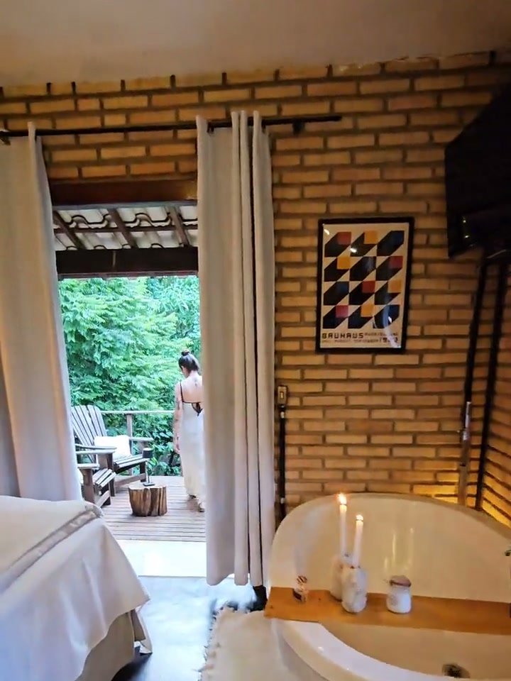 A banheira do Chalé Jacarandá Mata com velas acesas, e a porta aberta para a varanda e a mata
