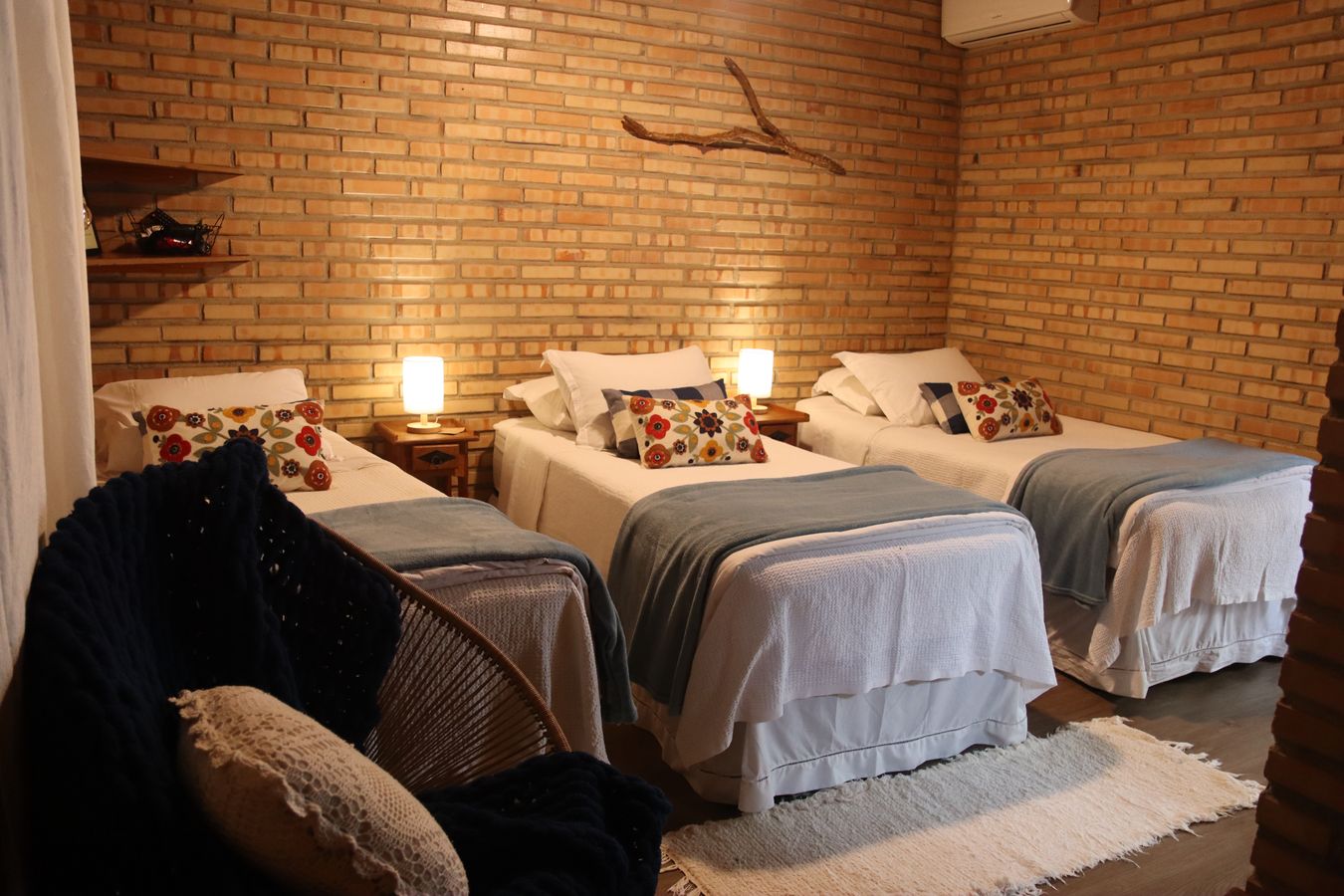 Quarto do Chalé das Vovós com três camas de solteiro e a poltrona de fio perto da porta