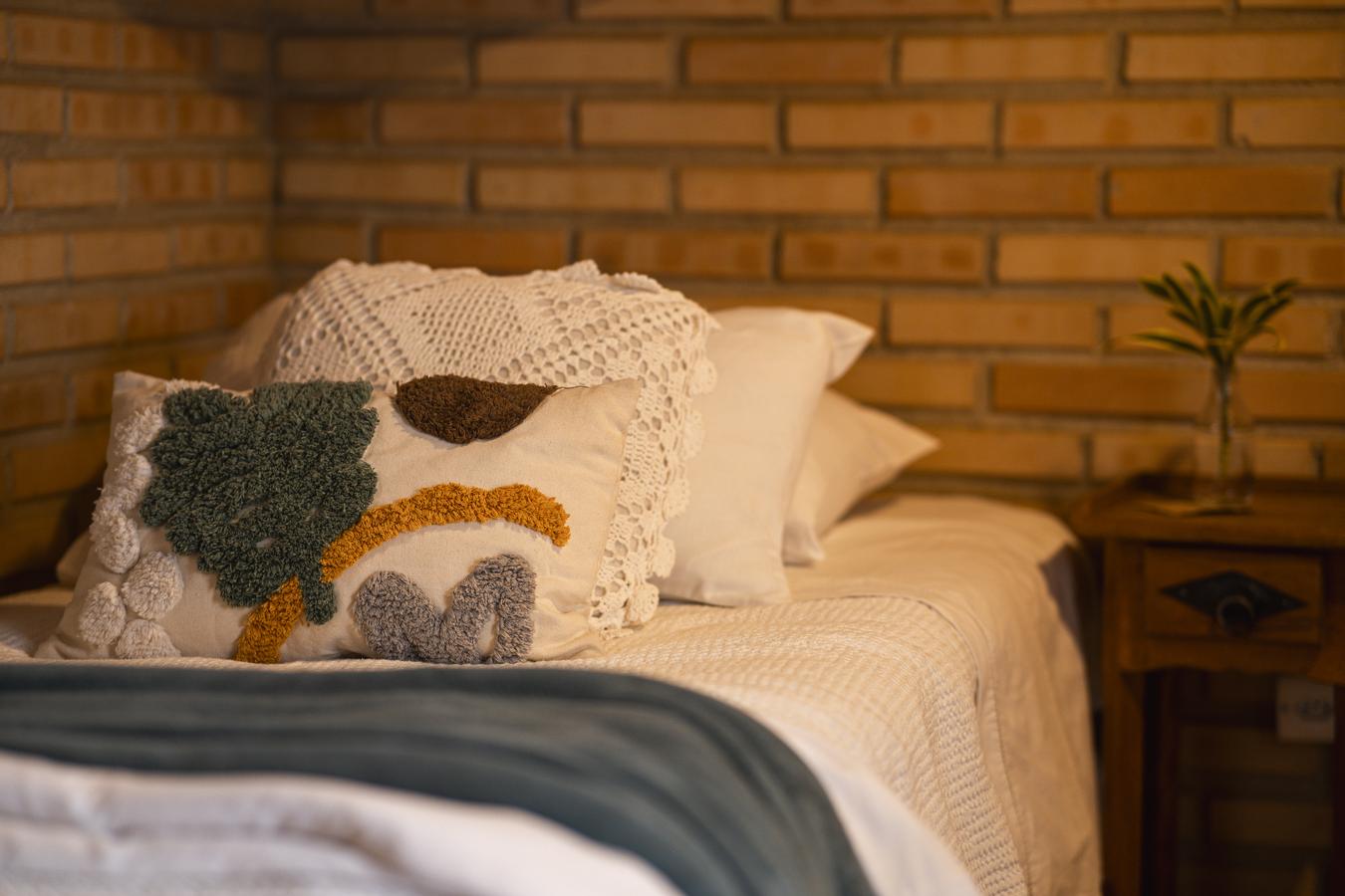 A cama posta do Chalé das Vovós, as almofadas bordadas e o tijolo aparente