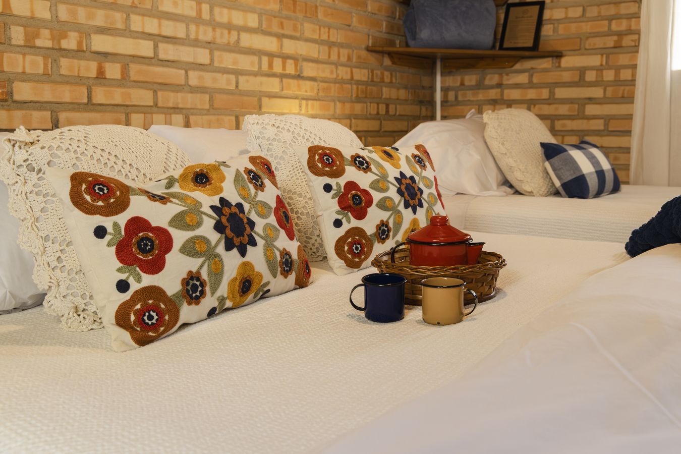 Almofadas bordadas de flores sobre a cama, com duas canecas esmaltadas