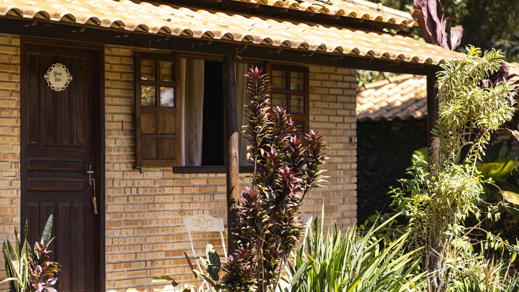 A fachada de um Chalé das Vovós, a porta de madeira e o telhado entre as plantas