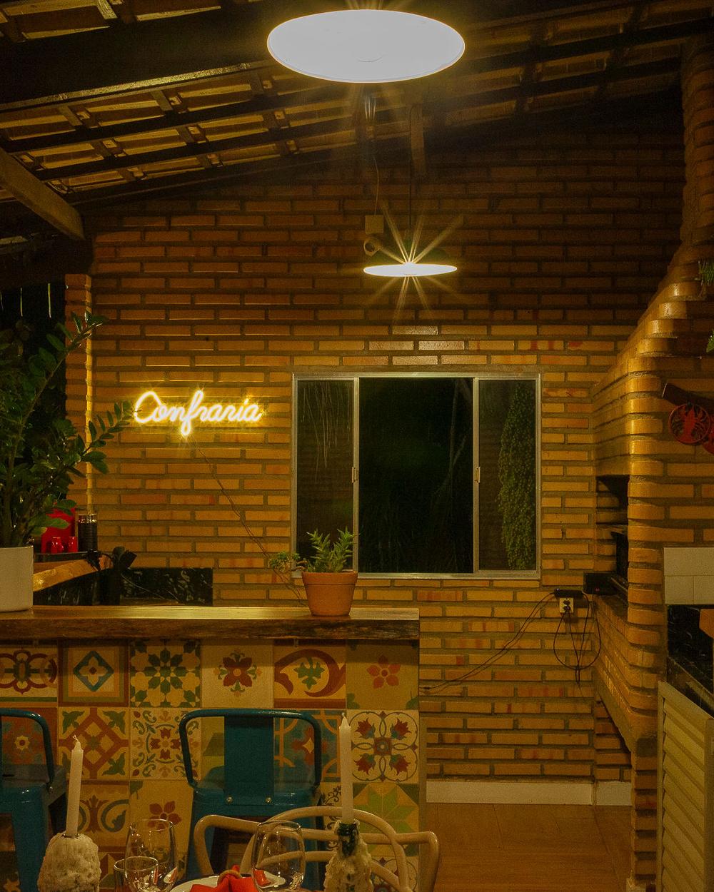 O salão da casa à noite, de tijolo aparente, com as luzes acesas