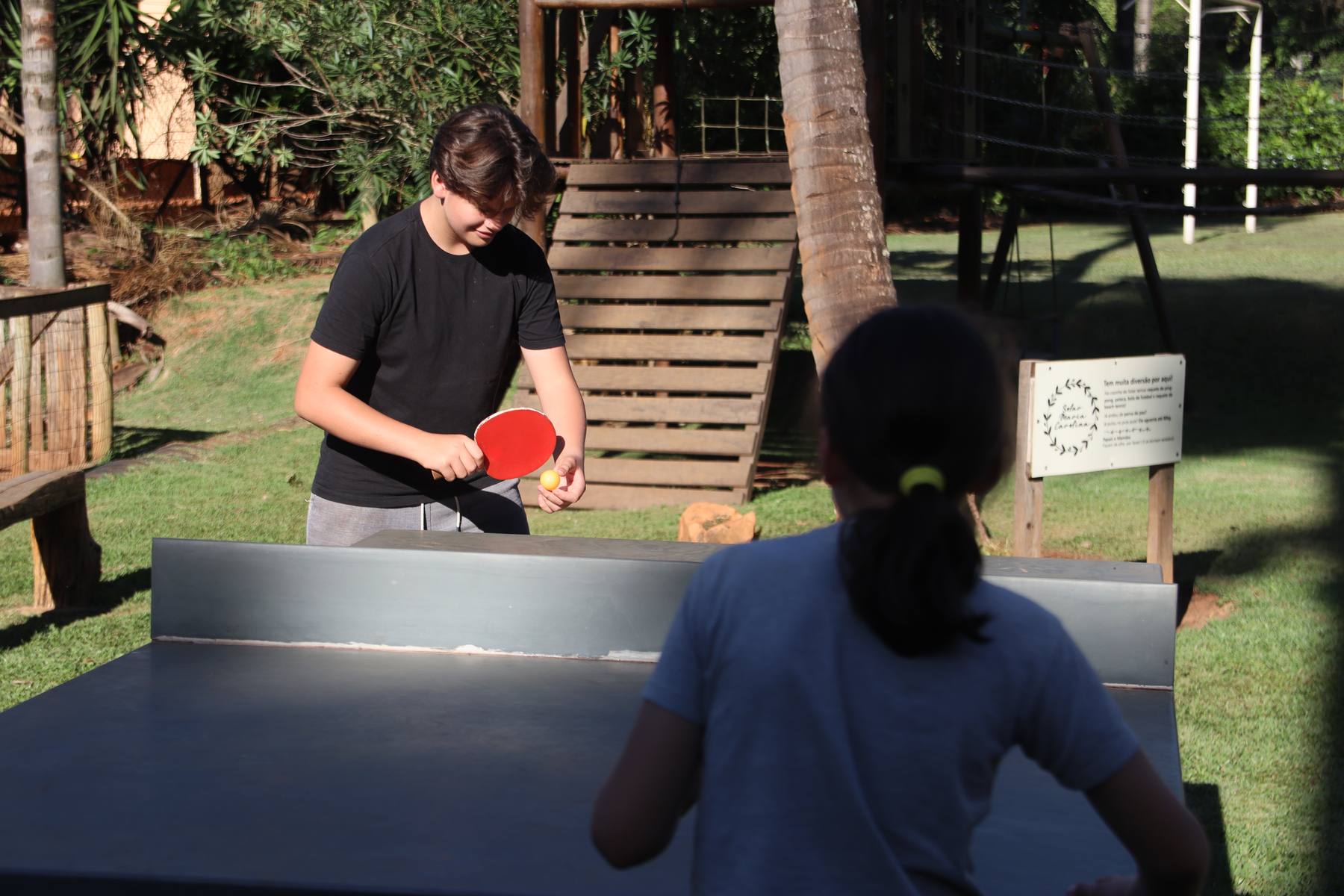 Dois hóspedes jogando pingue-pongue na mesa sob as árvores