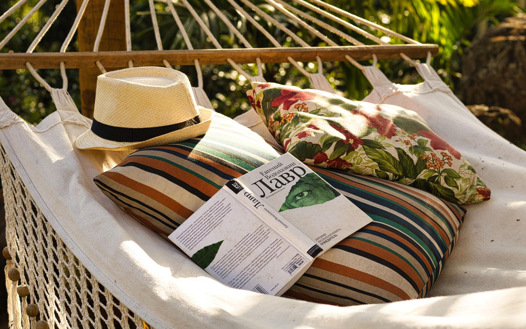 A rede armada à sombra, com um chapéu de palha, almofadas listradas e um livro aberto